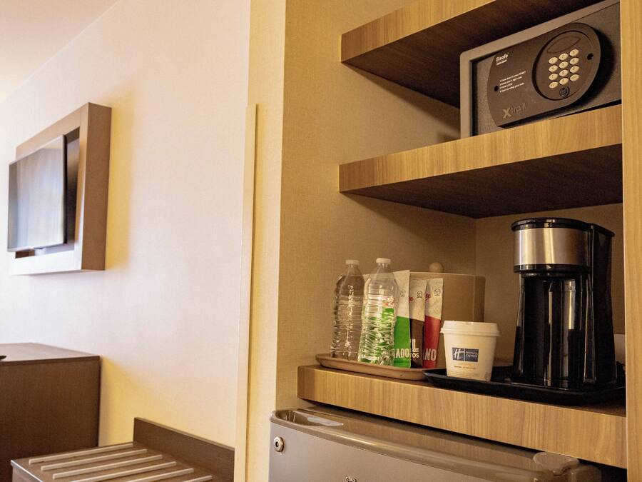 Quarto de hotel com minibar, televisão fixada na parede e máquina de café no balcão.