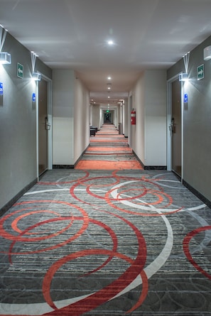 Un couloir d’hôtel avec un tapis à motifs, des portes de chaque côté et des panneaux indicateurs.