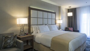 Une chambre d’hôtel avec un grand lit, deux tables de chevet avec des lampes, une chaise et une vue sur l’extérieur par une fenêtre munie de rideaux.