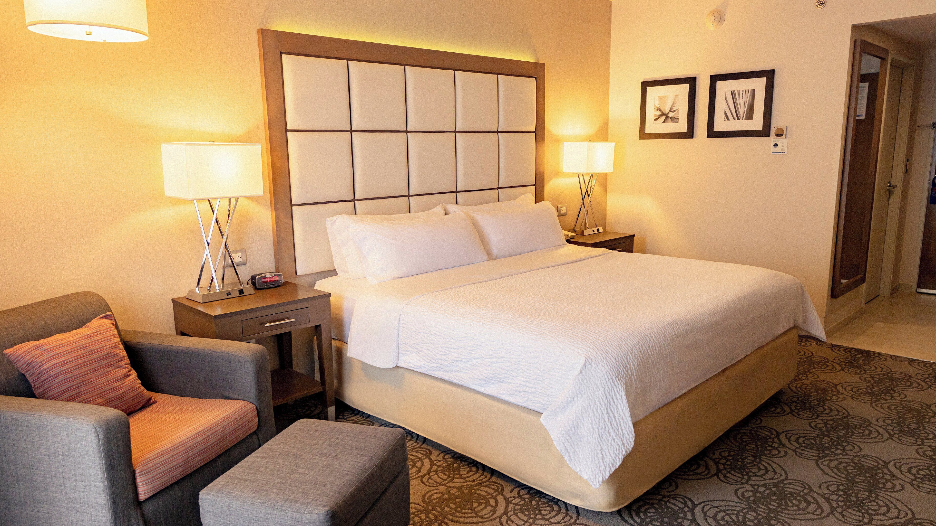 Una camera d'albergo con un letto grande, due comodini con lampade, una poltrona e un tappeto decorato.