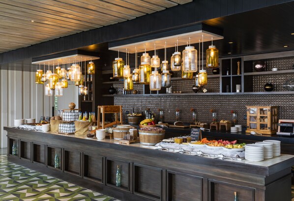 A buffet setup with hanging light fixtures, a variety of food items, and a patterned floor. - The Cape, A Thompson Hotel, by Hyatt (Cabo San Lucas)