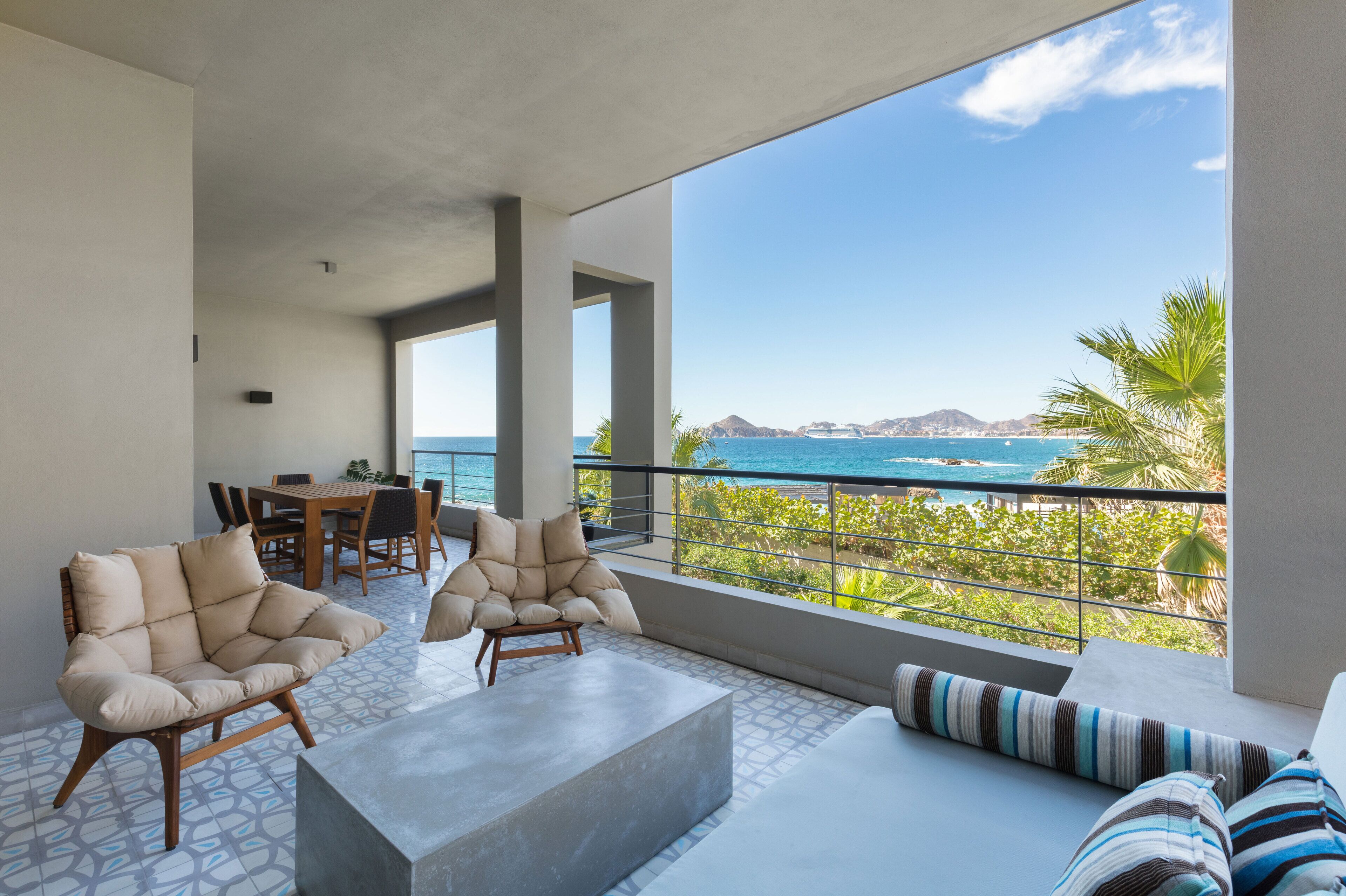A balcony with a view of the ocean, a dining area, and seating with a view.