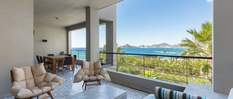 A balcony with a view of the ocean, a dining area, and seating with a view.