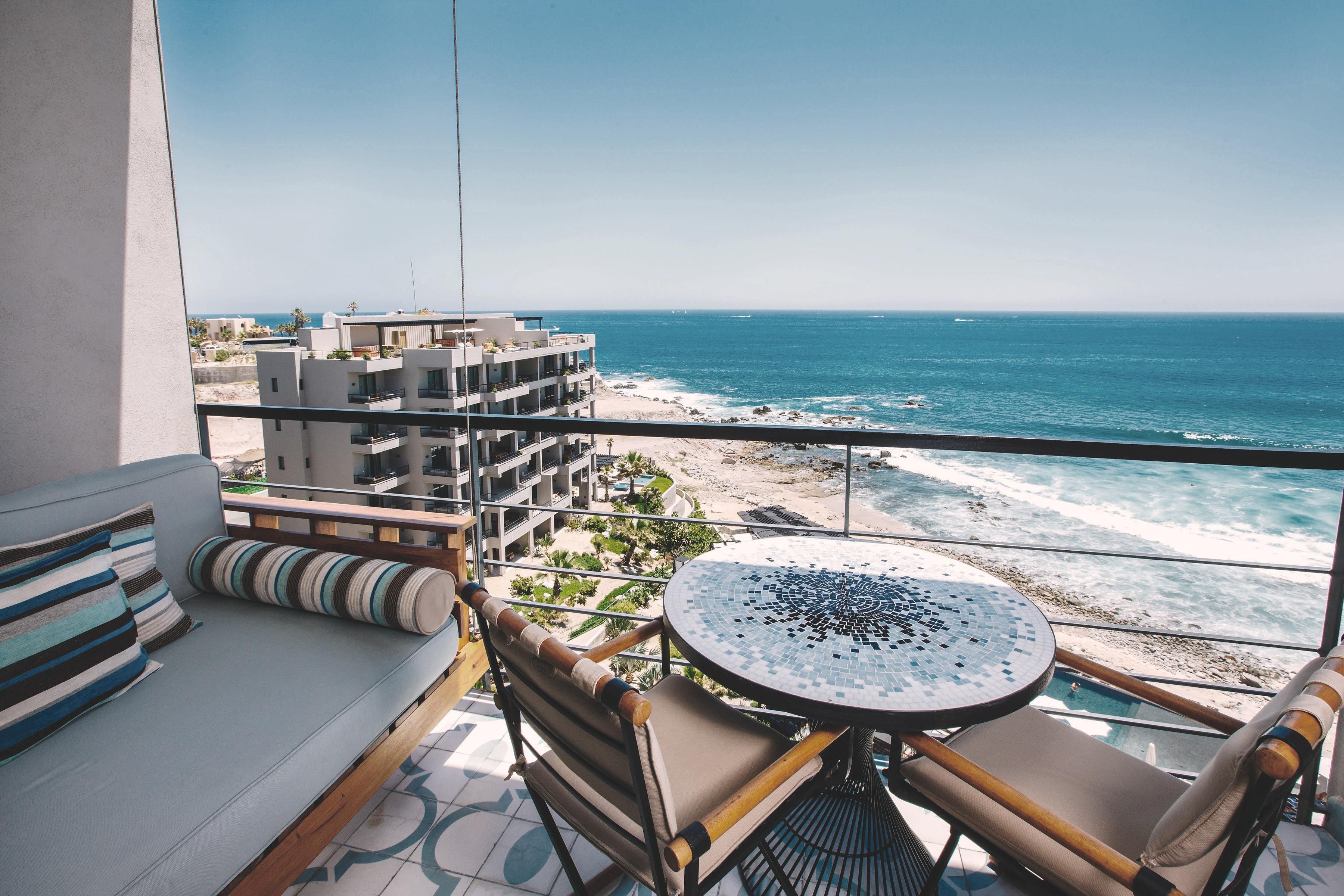 A balcony with a view of the ocean, a round table, and a sofa with striped cushions.