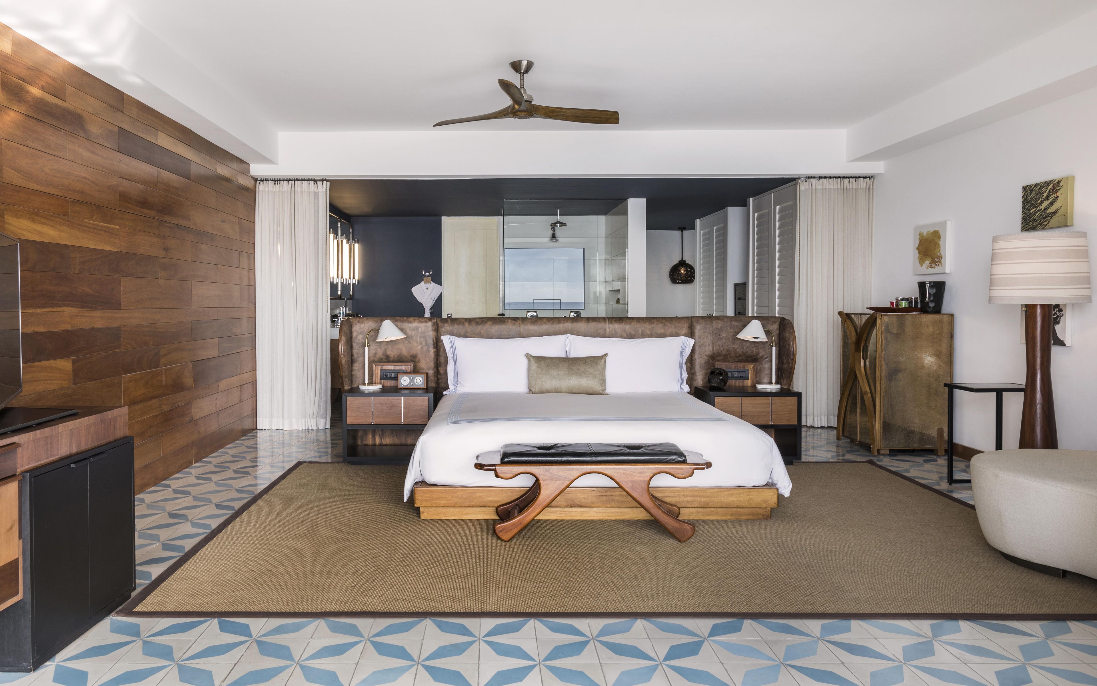 A hotel room with a bed, bedside tables, a ceiling fan, a wardrobe, and a mirror.