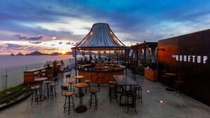 An outdoor bar area with a view of the sunset over the water, tables, chairs, and a sign reading "THE ROOFTOP". - The Cape, A Thompson Hotel, by Hyatt (Cabo San Lucas)