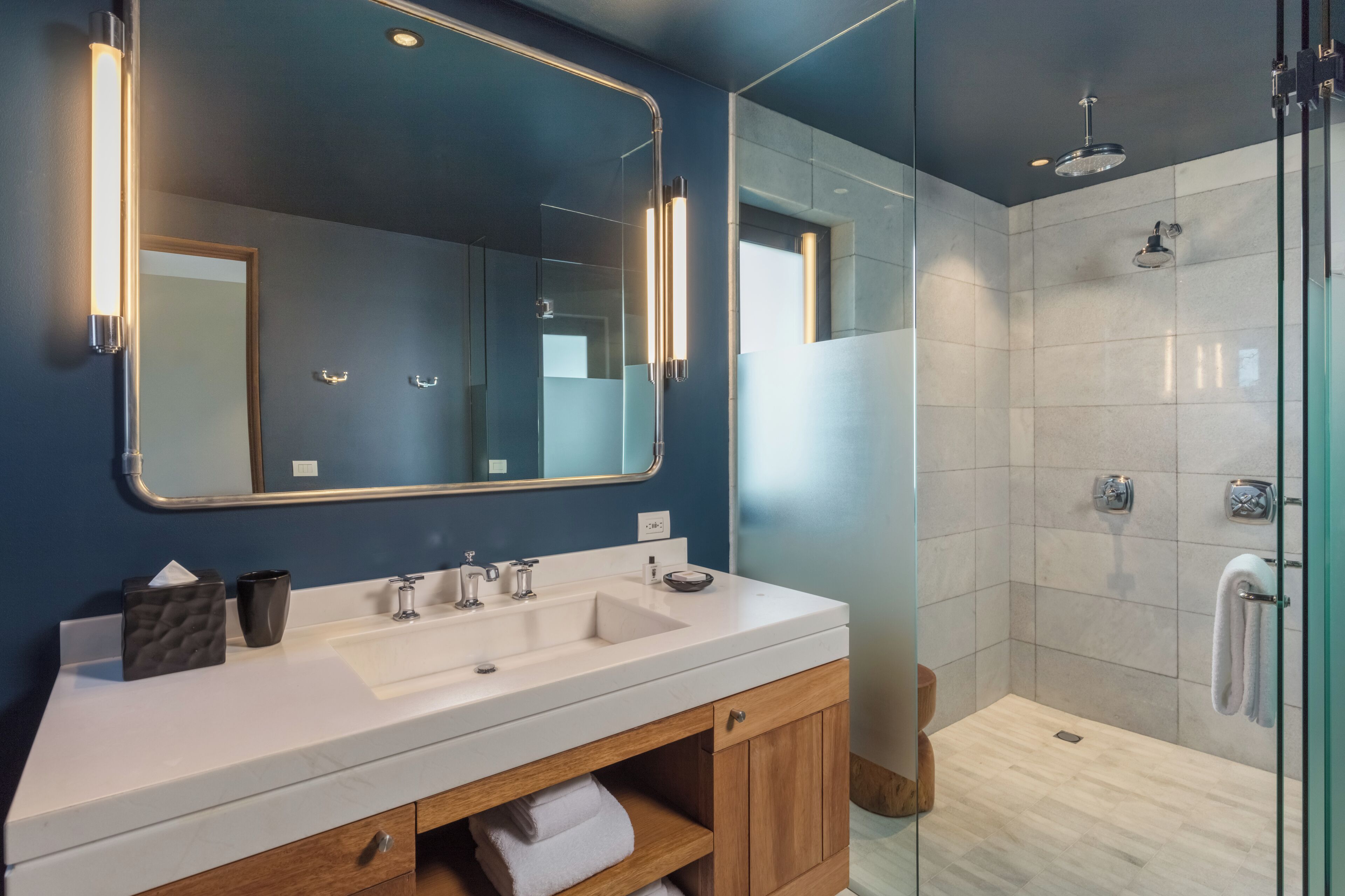 A modern bathroom with a large mirror, two sinks, and a glass-enclosed shower area.