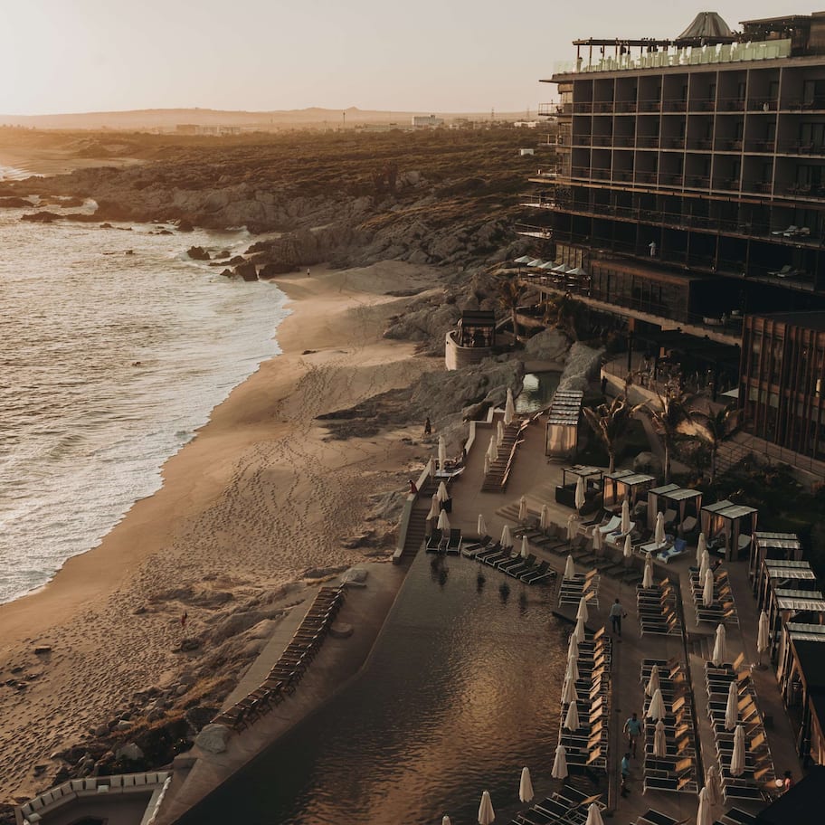A beachfront hotel with a pool, sun loungers, and a view of the ocean.