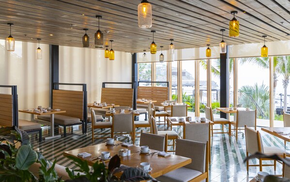 A modern restaurant with wooden furniture, glass tables, and hanging pendant lights. - The Cape, A Thompson Hotel, by Hyatt (Cabo San Lucas)