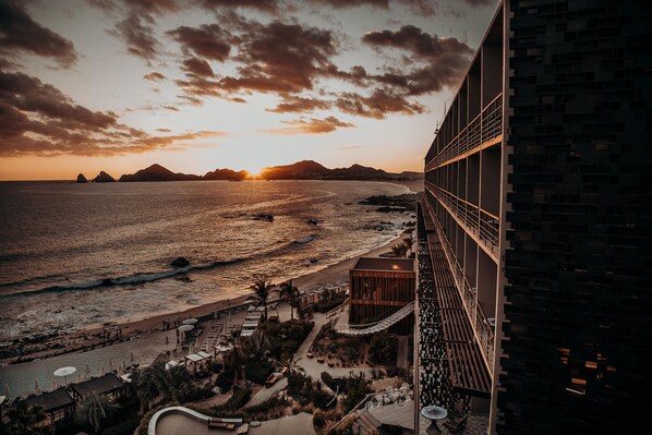 Un hôtel situé sur la côte, offrant une vue sur la mer et les montagnes au coucher du soleil.