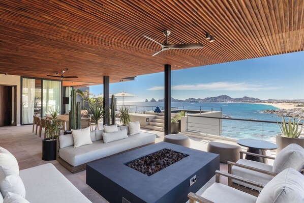 Un espacio exterior moderno con techo de madera, un brasero y vista al océano.