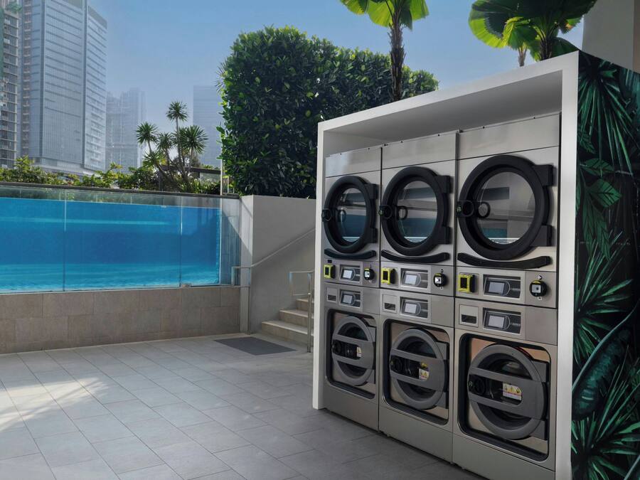 Eine Wäscherei mit mehreren Waschmaschinen, ein Pool und Blick auf hohe Gebäude.