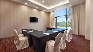A conference room with a long table, six chairs, a flat-screen TV, and large windows with curtains.