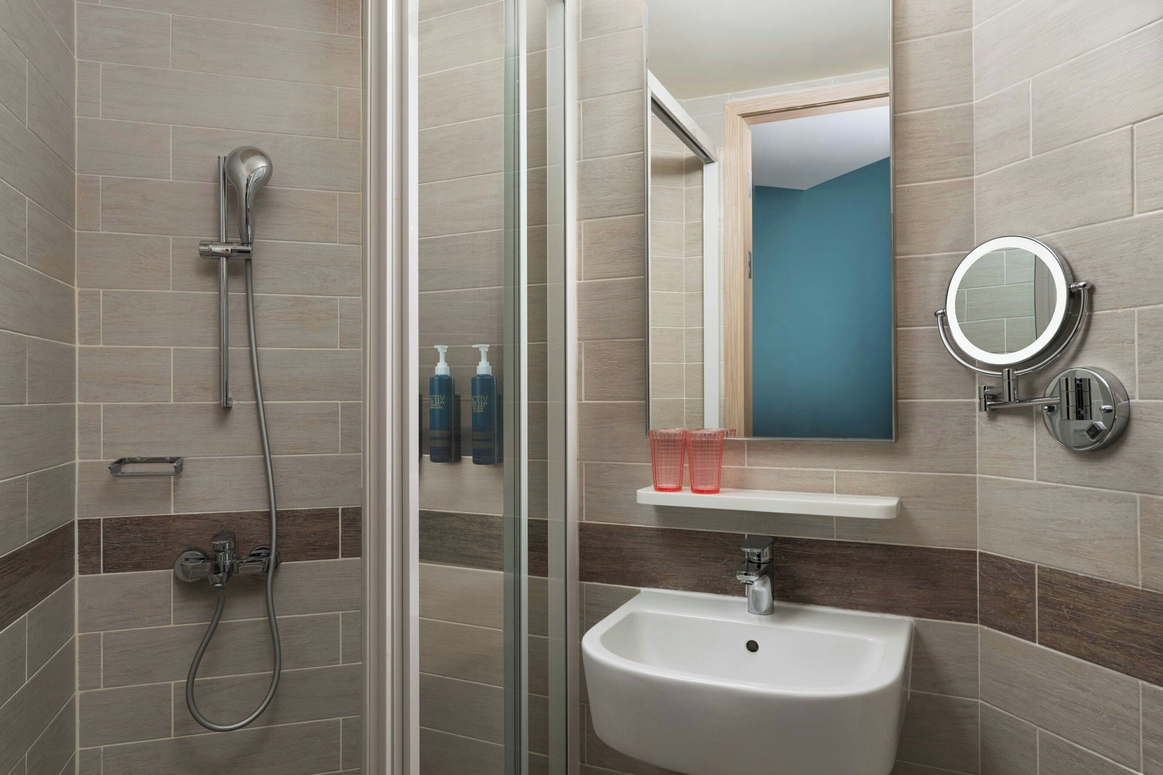Une salle de bain moderne avec une douche à parois de verre, un lavabo blanc et un miroir doté d’un cadre rond.