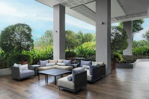 A spacious outdoor seating area with multiple sofas and a coffee table, surrounded by lush greenery and a view of the sky.