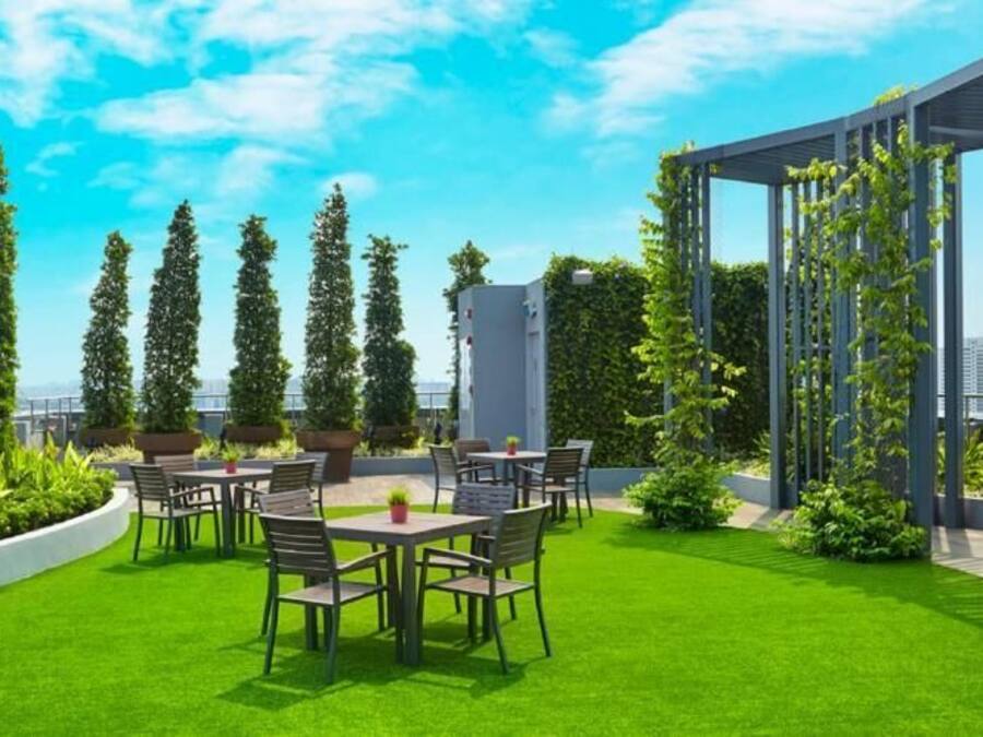 A rooftop terrace with green grass, outdoor seating, and tall trees.