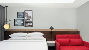 A hotel room with a bed, a red sofa, a nightstand, and wall art.