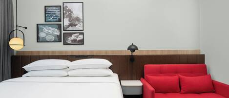 A hotel room with a bed, a red sofa, a nightstand, and wall art.