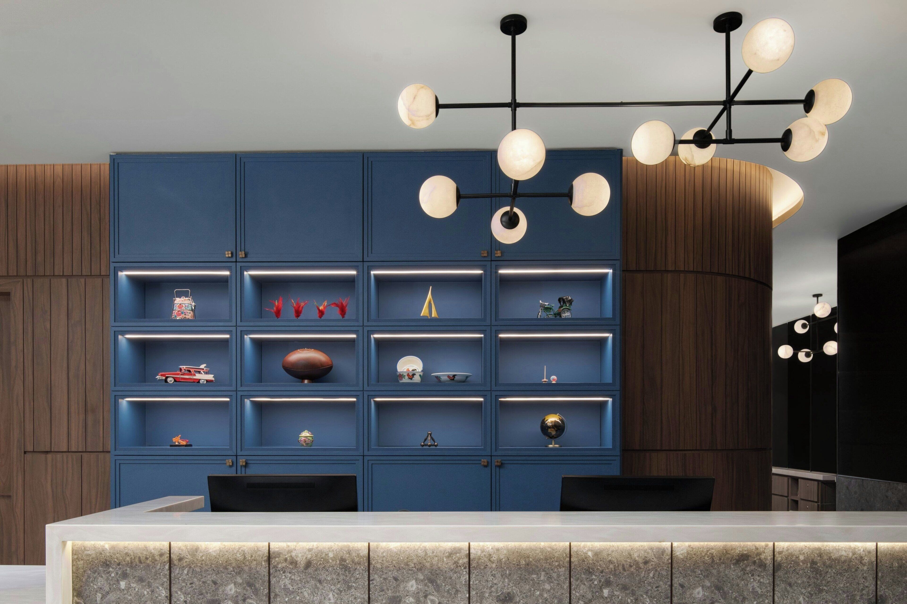Une cuisine moderne dotée d’un îlot central, d’étagères intégrées ornées de divers objets décoratifs et d’un luminaire contemporain.