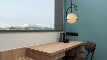 A modern room with a wooden desk, a chair, a hanging light fixture, and a view of a cityscape through a large window.