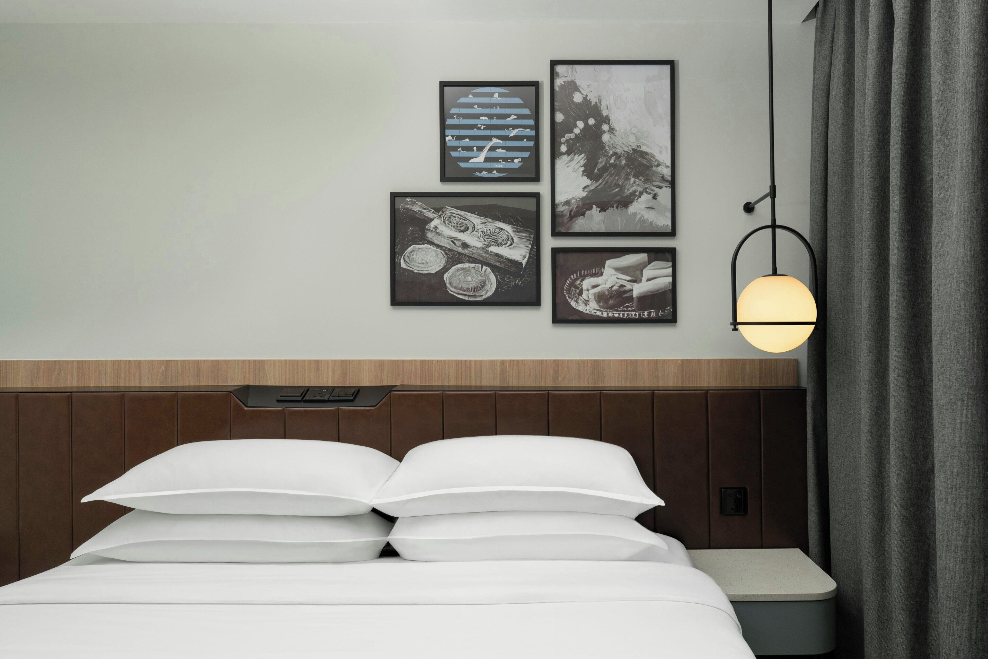 Habitación de hotel con una cama, una mesita de noche, una lámpara de pared y tres obras de arte enmarcadas.