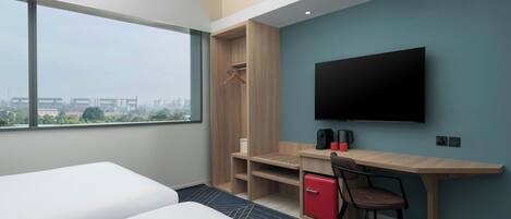 Habitación de hotel con dos camas, un escritorio, una silla, un televisor y vistas a la ciudad.