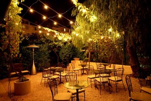An outdoor patio with tables and chairs, string lights, and a pergola covered in vines. - Hotel Royal Bon Repos (Sainte-Maxime)