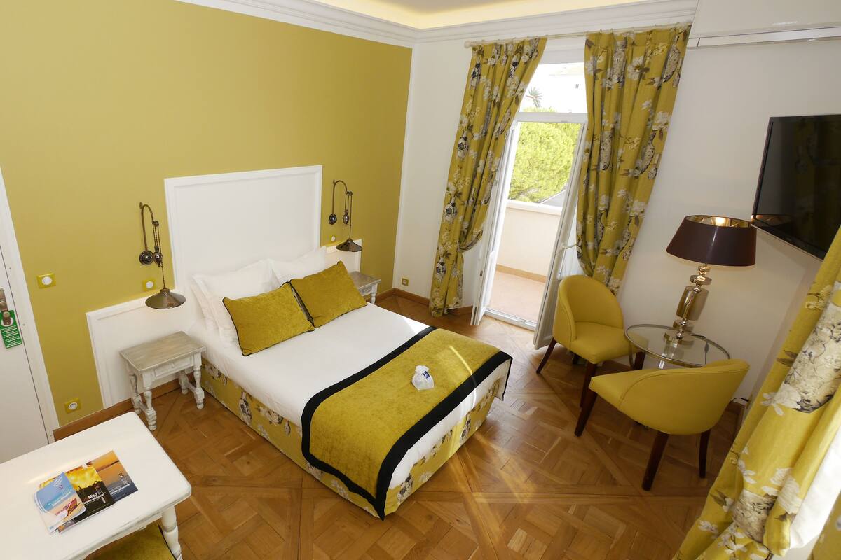 A hotel room with a bed, bedside table, lamp, chair, and a view of the outdoors.