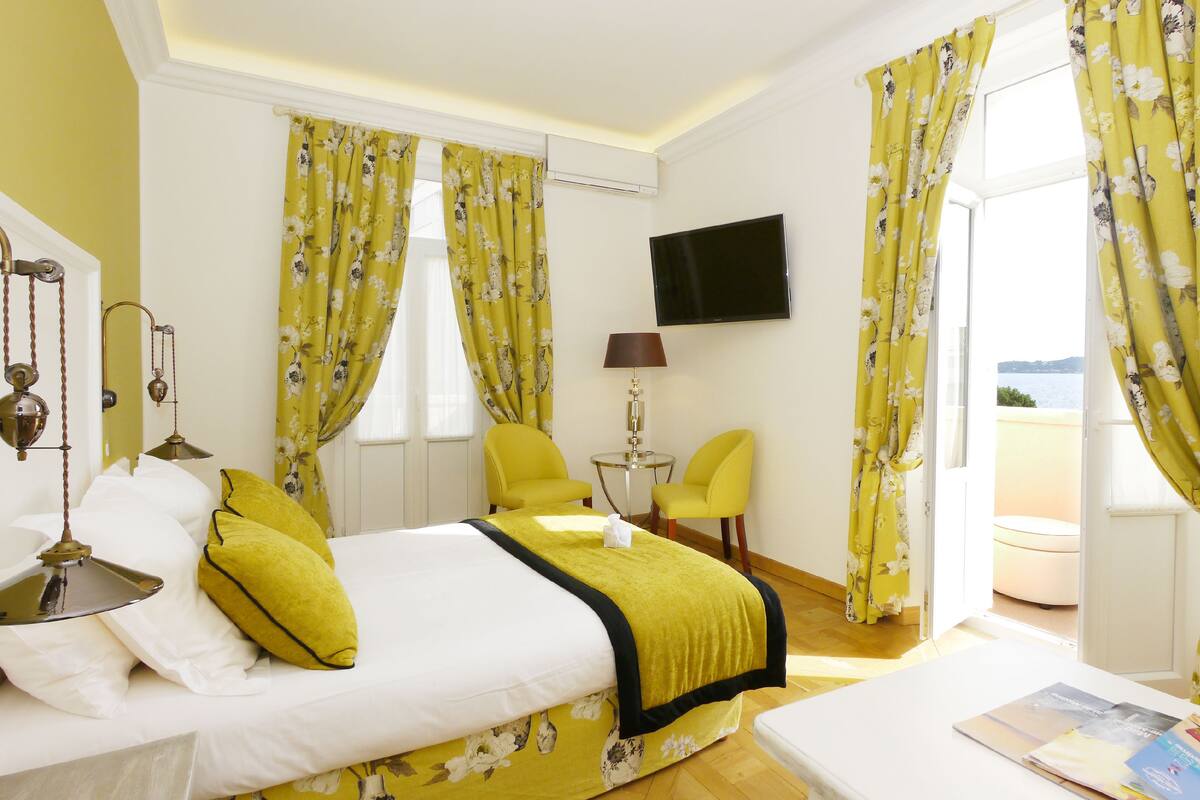 A hotel room with a bed, a desk, a chair, a TV, and a window with curtains.