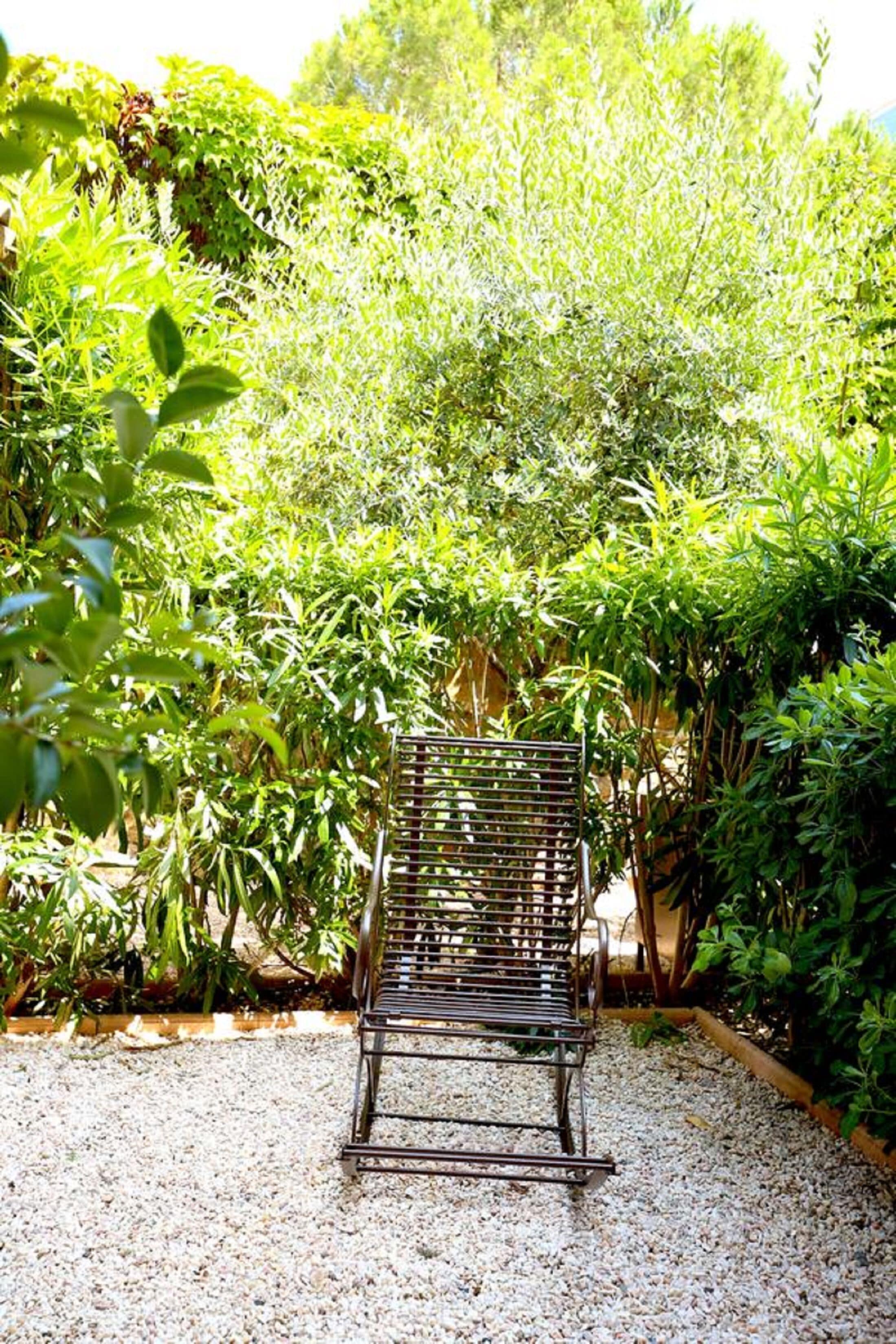 Een metalen bankje in een tuin met grind, omgeven door weelderige groene beplanting.