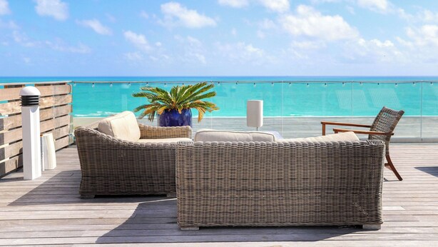 A wicker sofa and chair set on a wooden deck with a view of the ocean. - Nautilus Sonesta Miami Beach (Miami Beach)