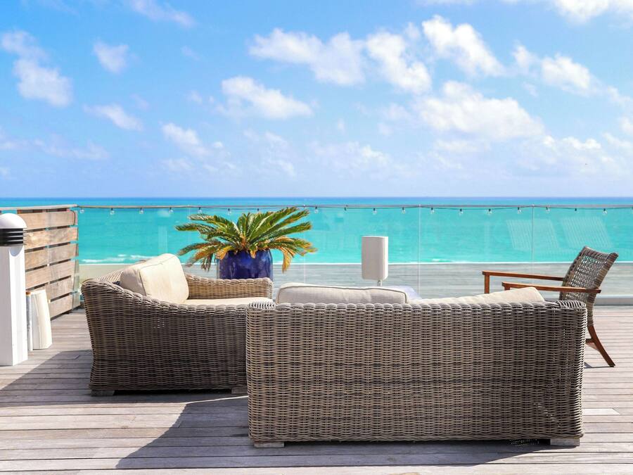 A wicker sofa and chair set on a wooden deck with a view of the ocean.