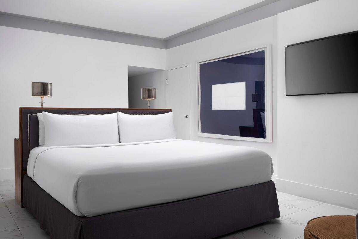 A modern hotel room with a large bed, a flat-screen TV mounted on the wall, and a window providing a view.