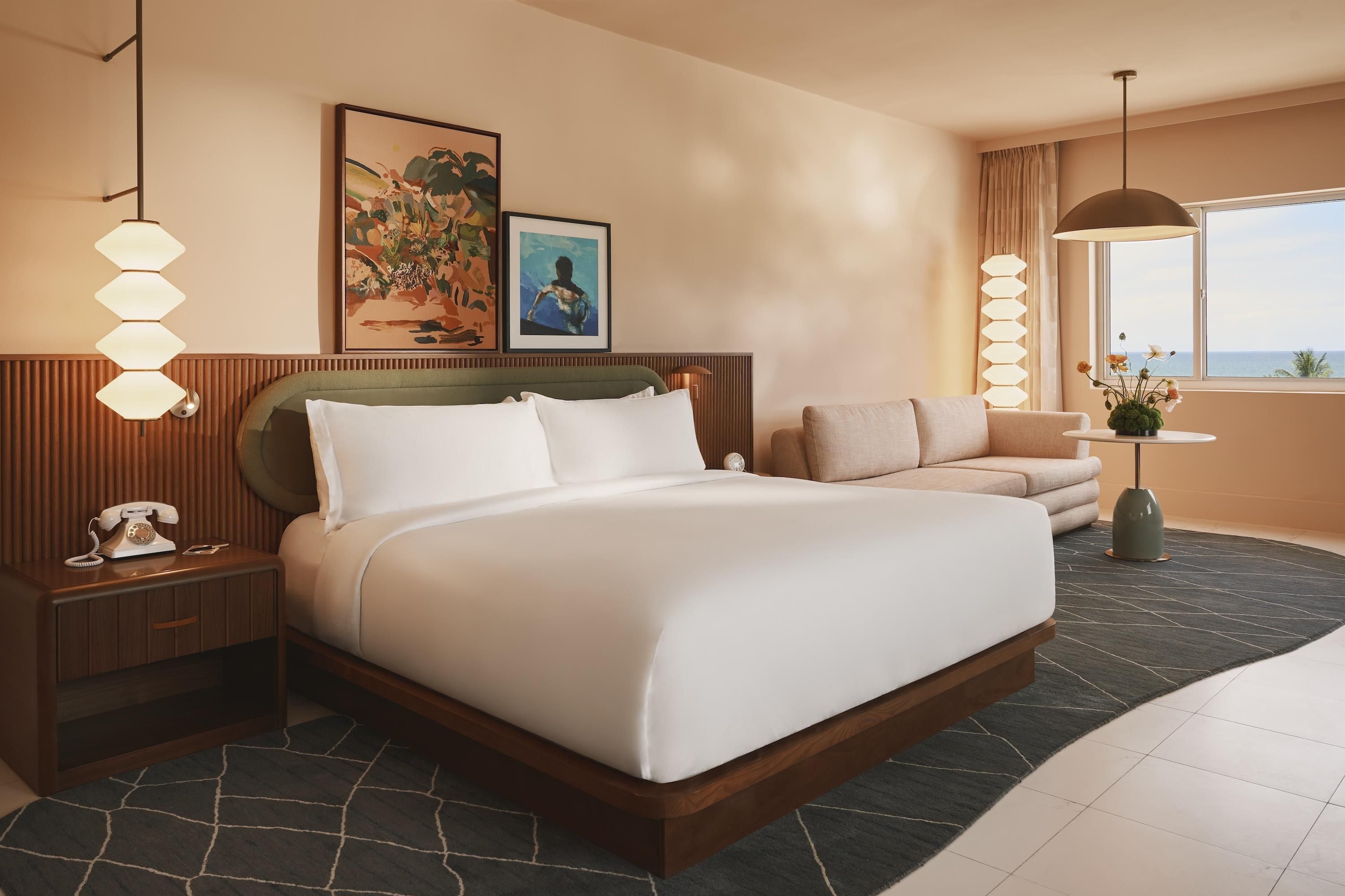 Habitación de hotel con una cama grande, un sofá, un escritorio con teléfono y una ventana con vistas.