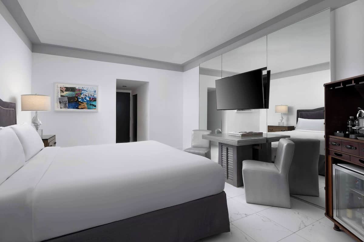 A modern hotel room with a large bed, a desk with a flat-screen TV, a chair, and a wardrobe.