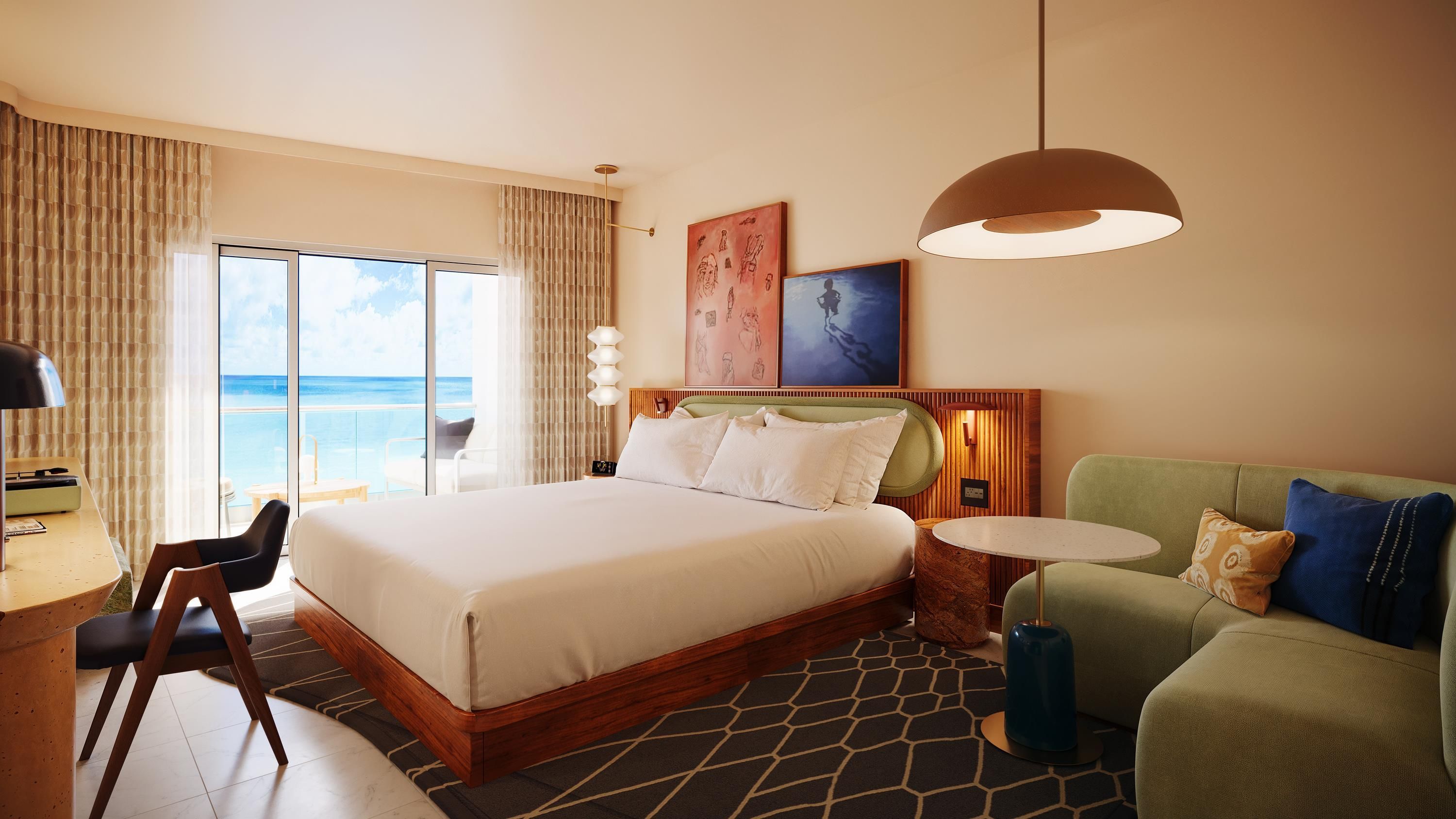 Ein Hotelzimmer mit einem großen Bett, einem grünen Sofa, einem kleinen Tisch und Blick auf den Ozean.