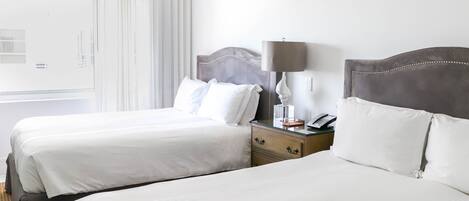 A hotel room with two beds, a nightstand with a lamp, and a window with curtains.