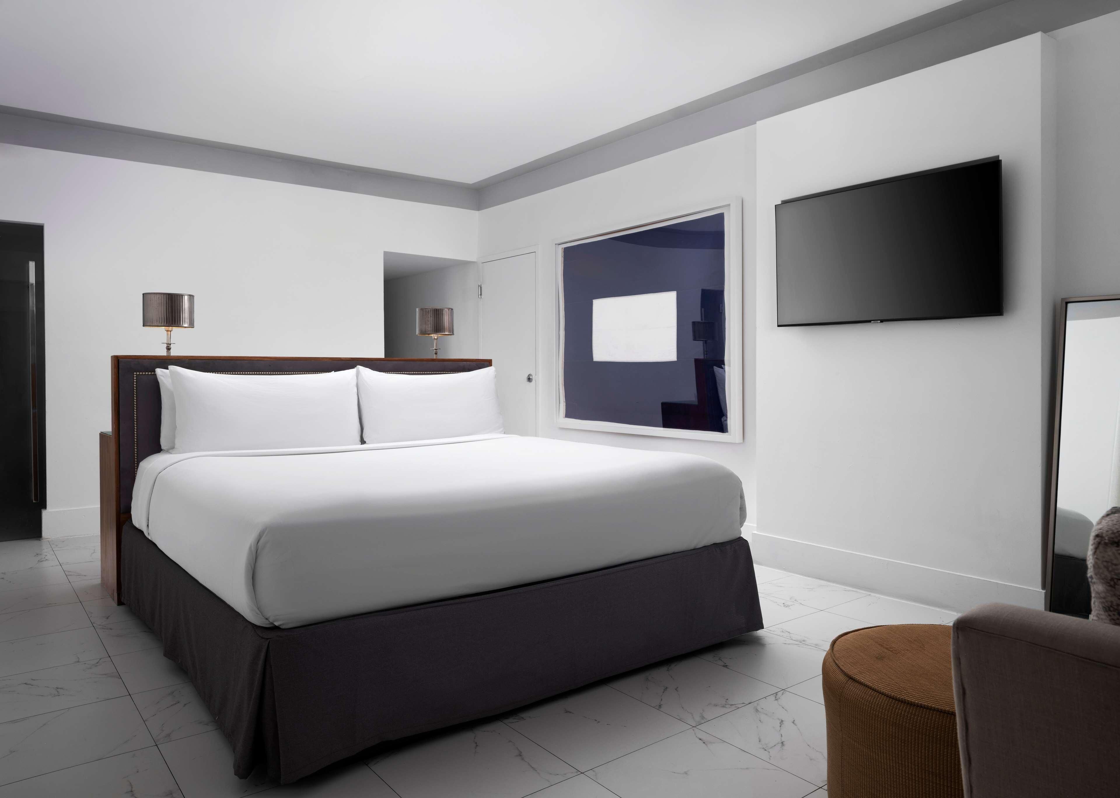 A modern hotel room with a large bed, a flat-screen TV, and a large window.