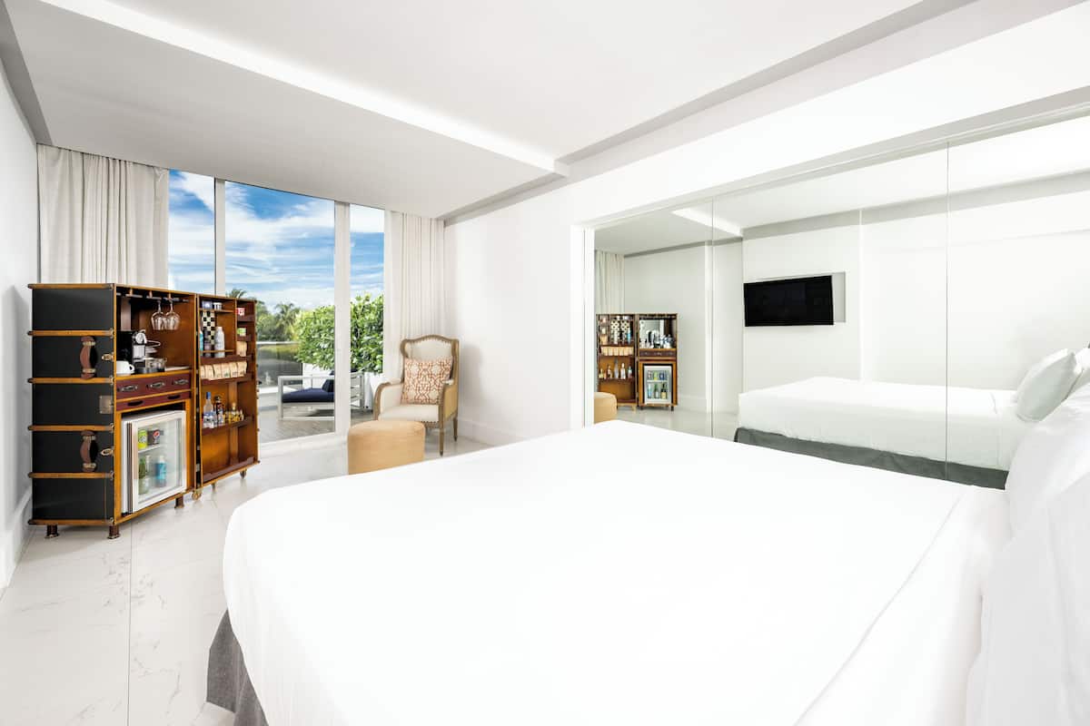 A modern hotel room with a large bed, a seating area with a chair, a wardrobe, and a television.