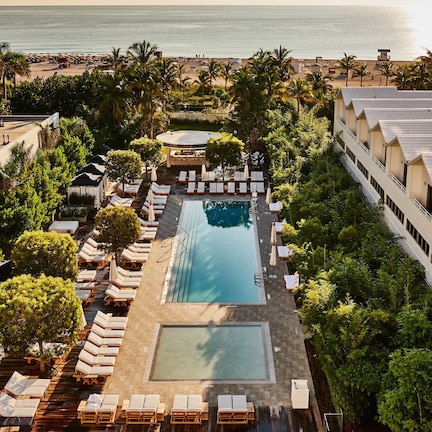 A resort with a central swimming pool, lounge areas, and a view of the ocean.