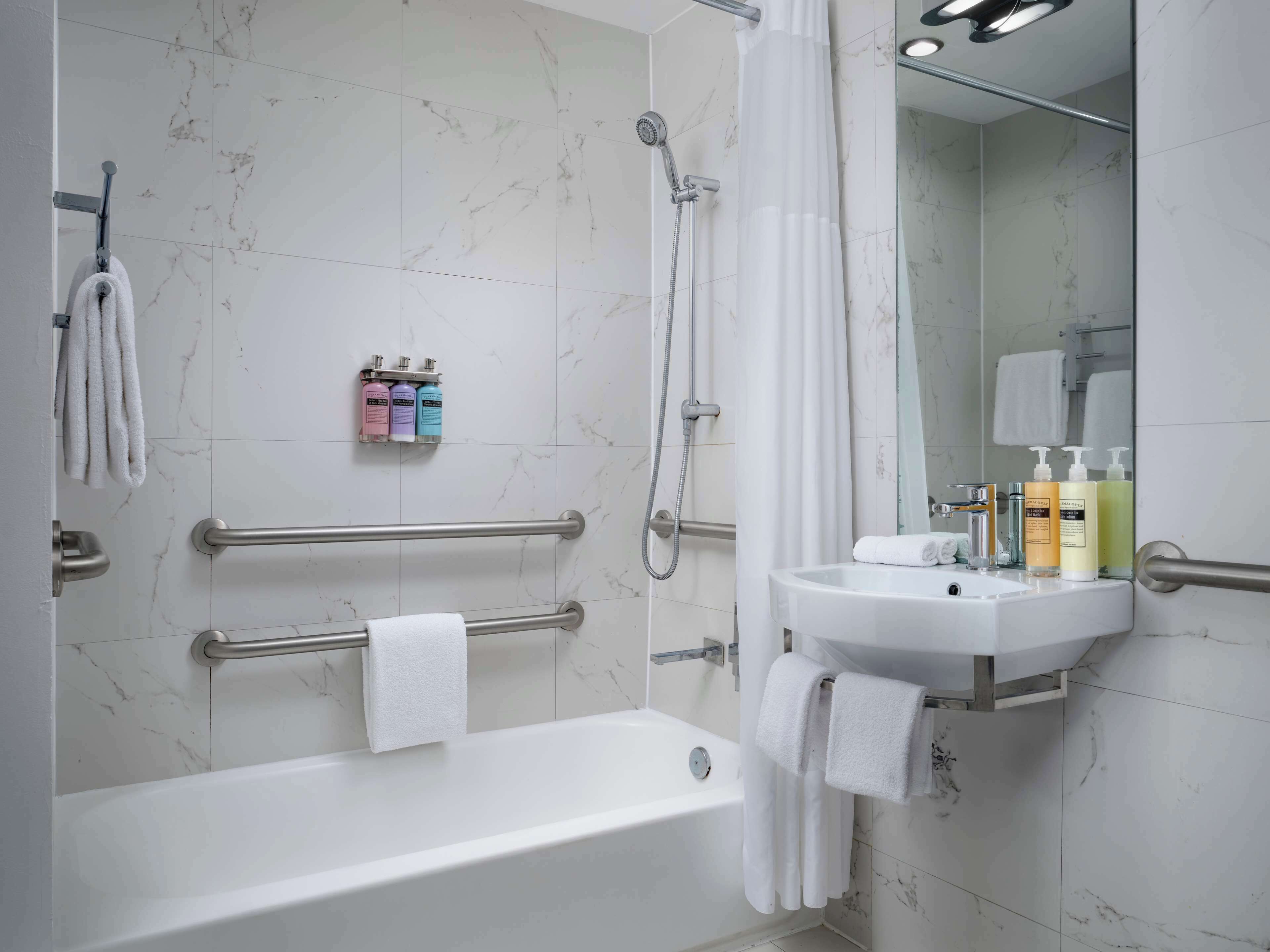 A modern bathroom with a bathtub, a shower, a vanity with toiletries, and a handrail for accessibility.
