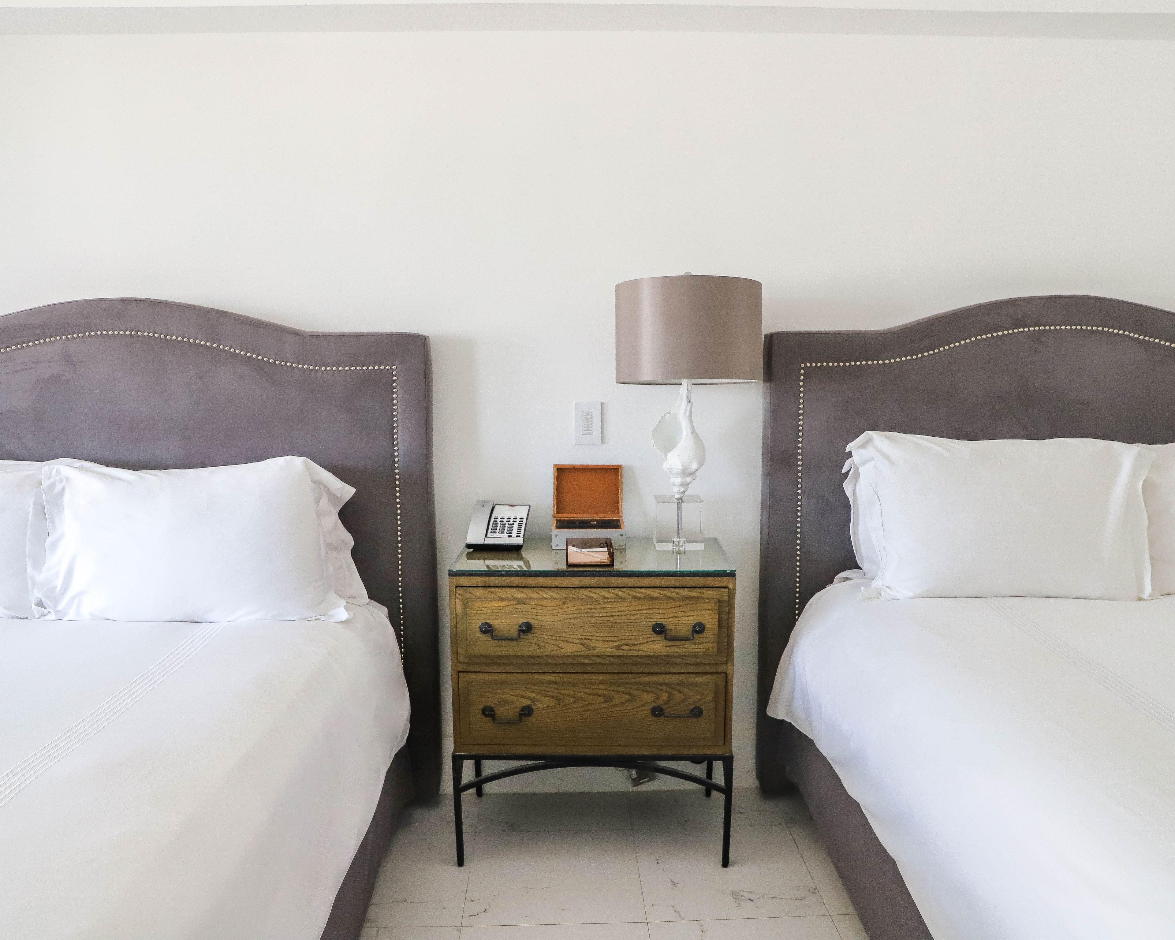 A hotel room with two beds, a nightstand with a lamp, and a small wooden dresser.