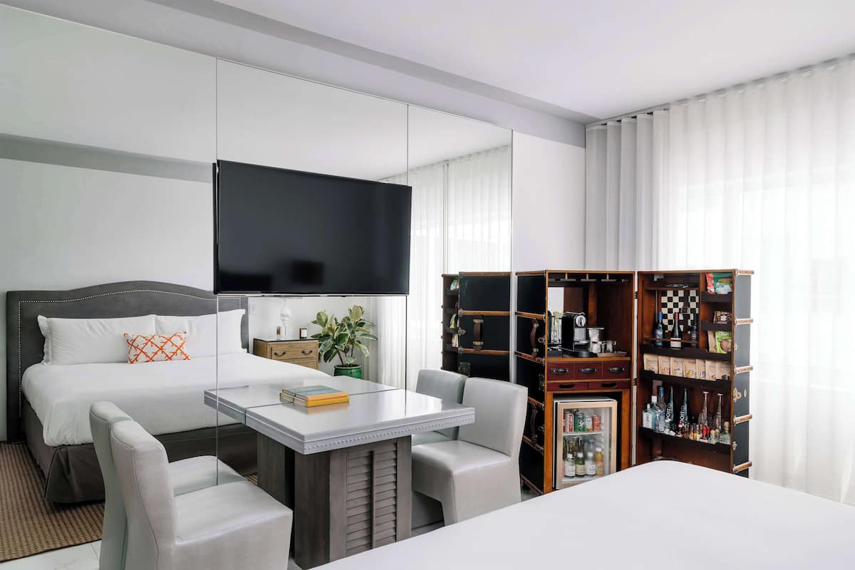 A hotel room with a bed, a desk, two chairs, a television, and a minibar.