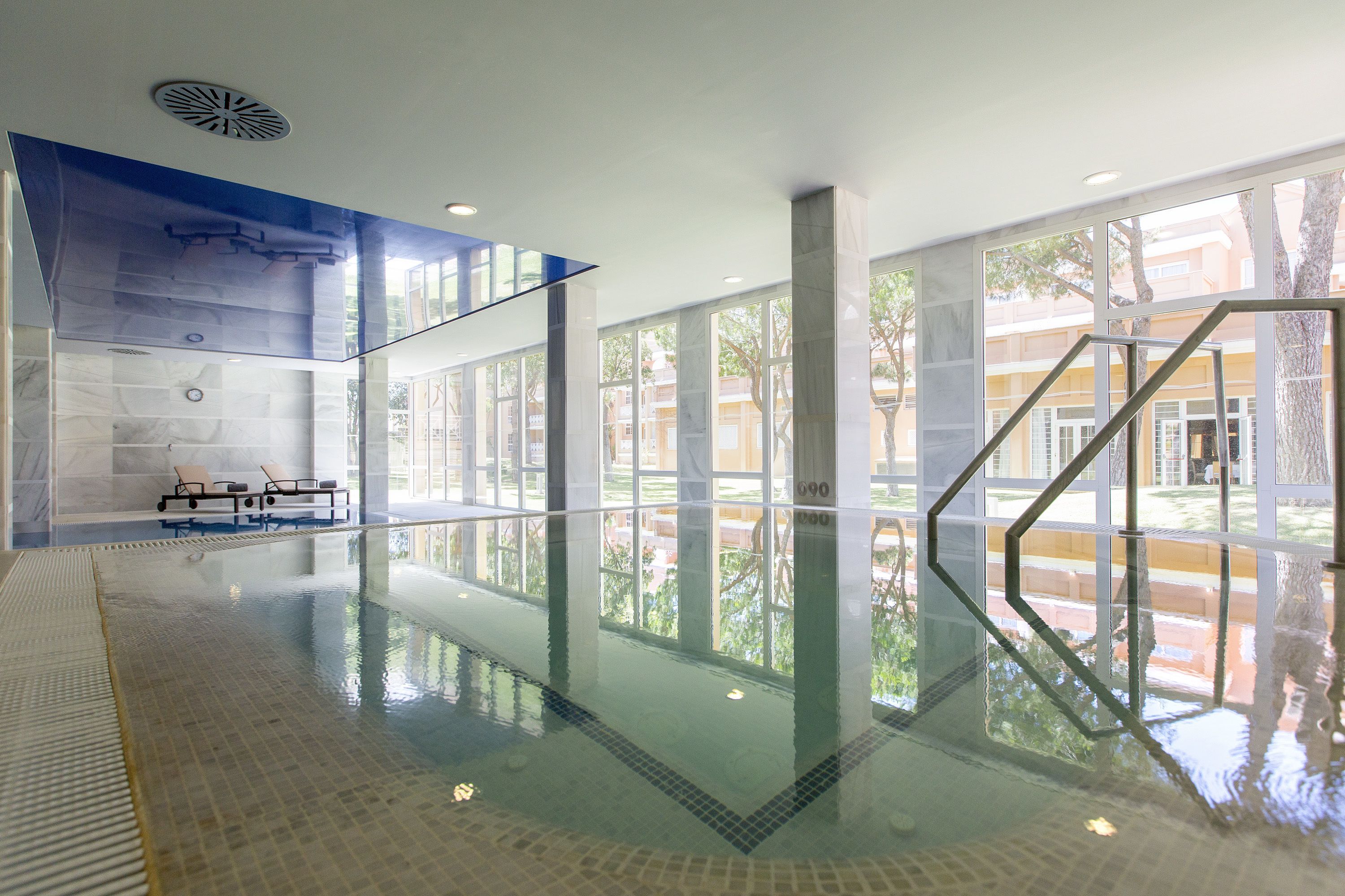 An indoor swimming pool with clear glass walls, a tiled floor, and a view of the outside.