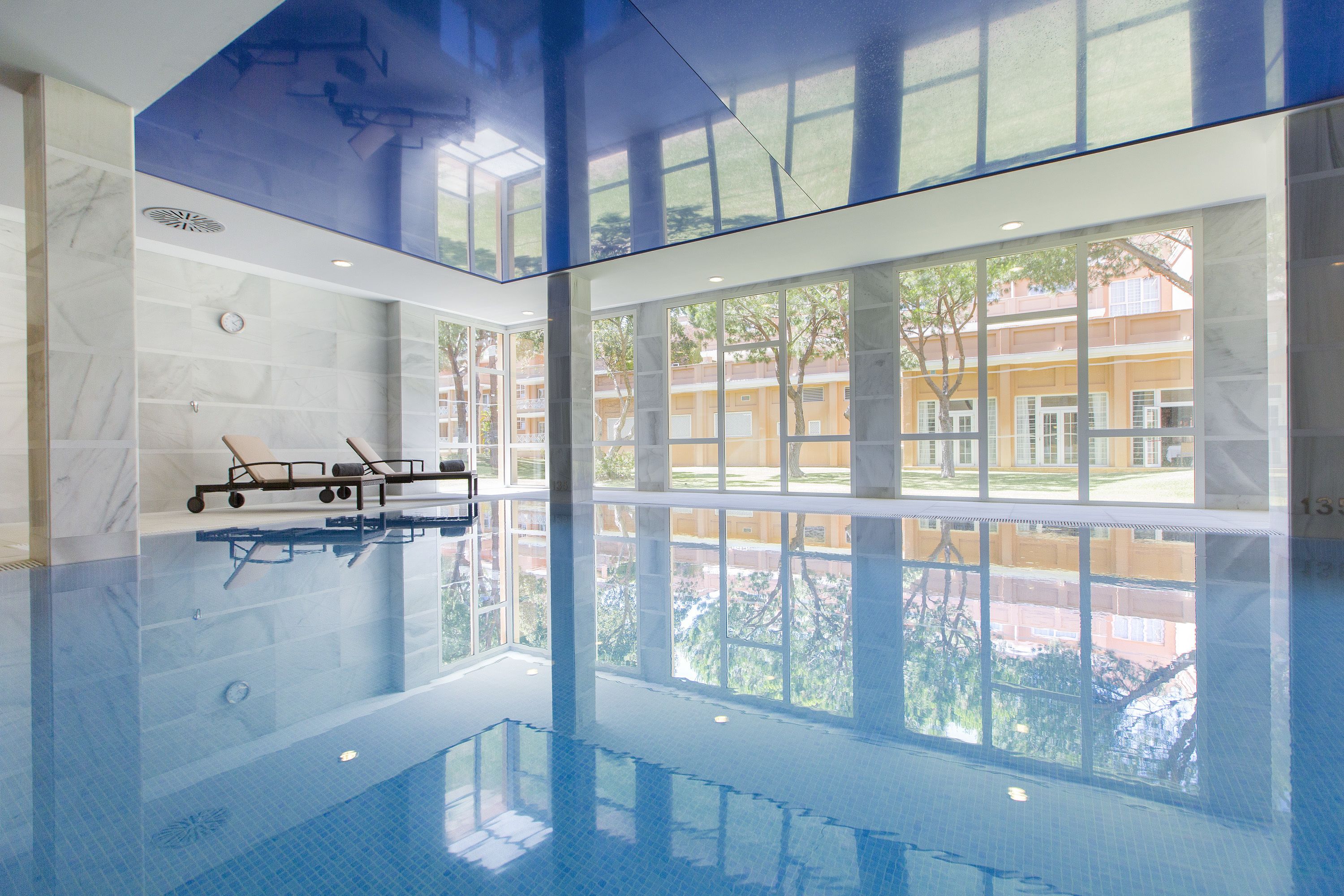 Una piscina interior con paredes de vidrio transparente, un trampolín y vistas a edificios cercanos.