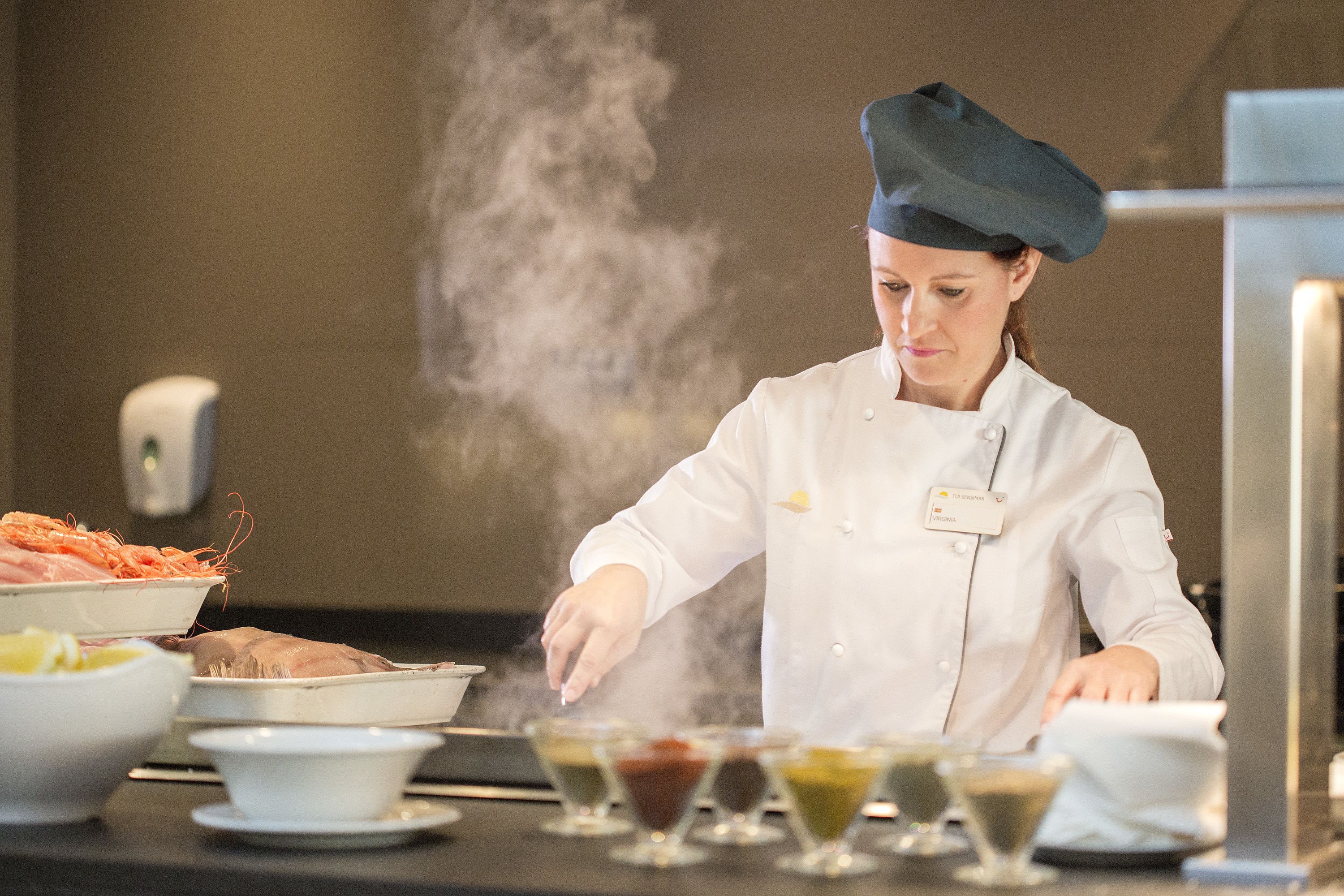 A chef in a white uniform and hat preparing dishes in a kitchen with various bowls and plates of food.