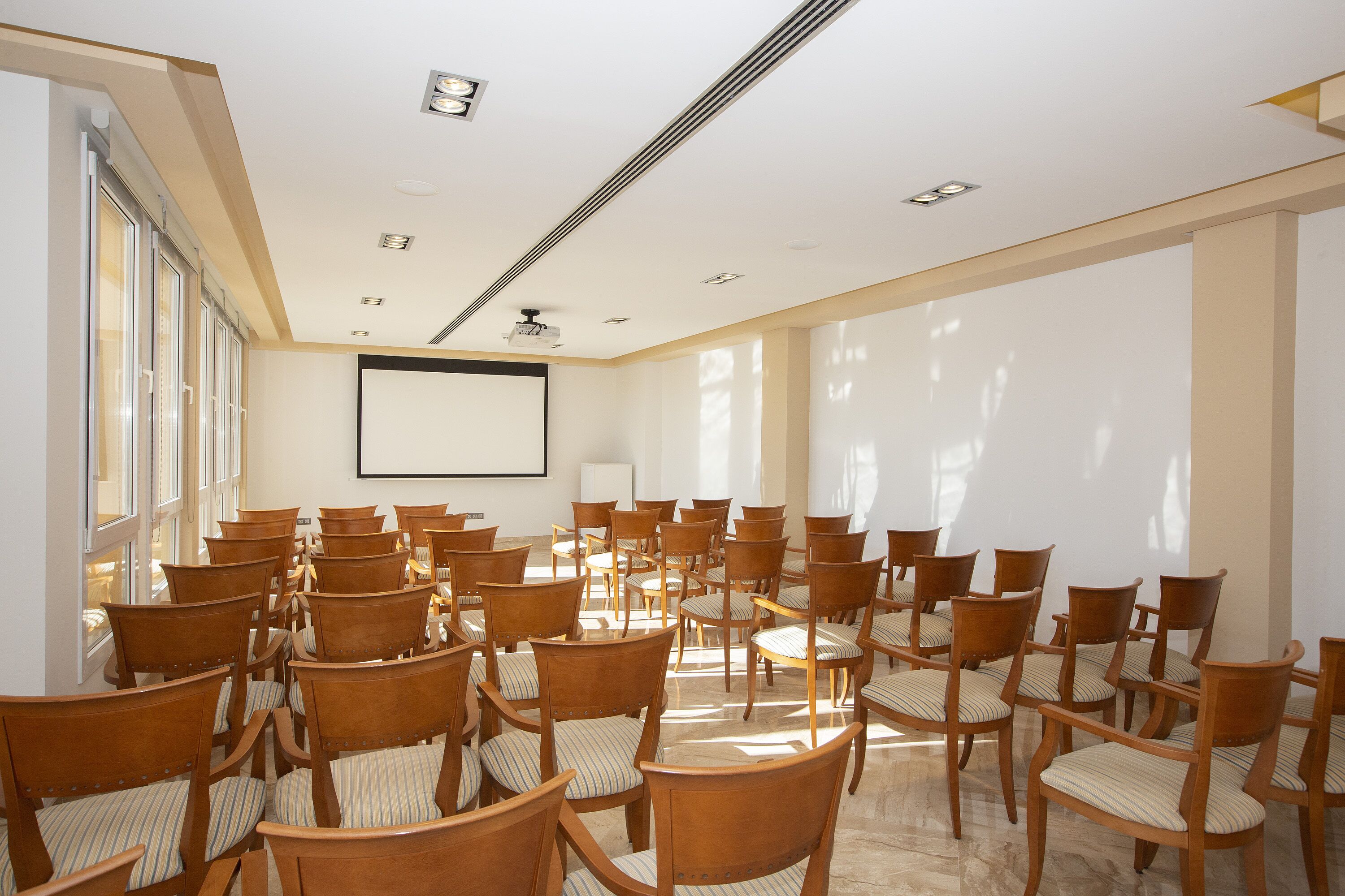 A conference room with rows of wooden chairs and a large screen at the front.