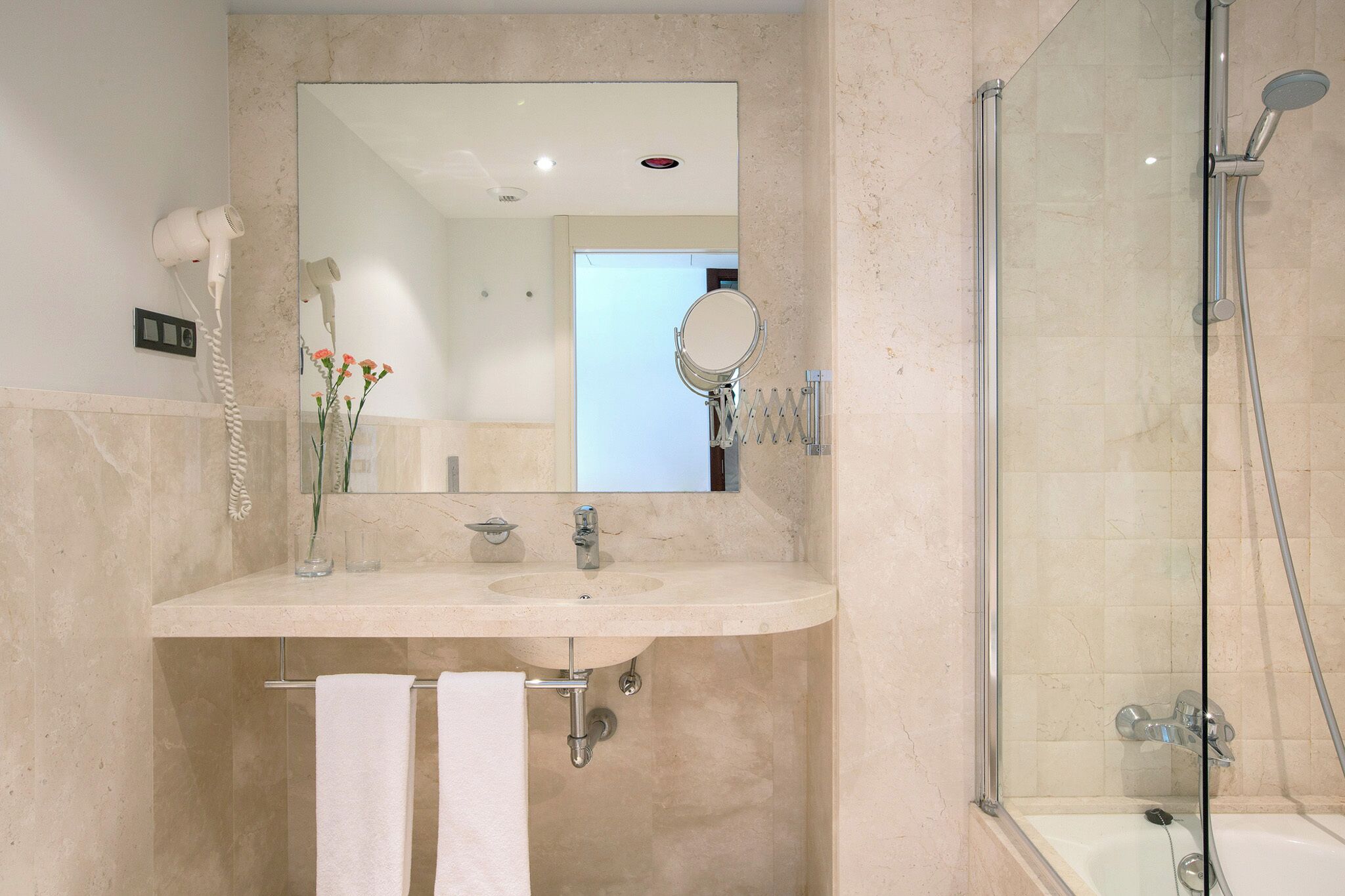 A modern bathroom with a marble sink, a hairdryer, a mirror, and a glass-enclosed shower.