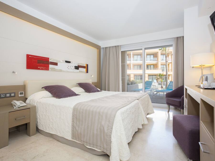 Ein Hotelzimmer mit einem großen Bett, einem Schreibtisch mit Lampe, einem Fernseher und Blick auf den Balkon.