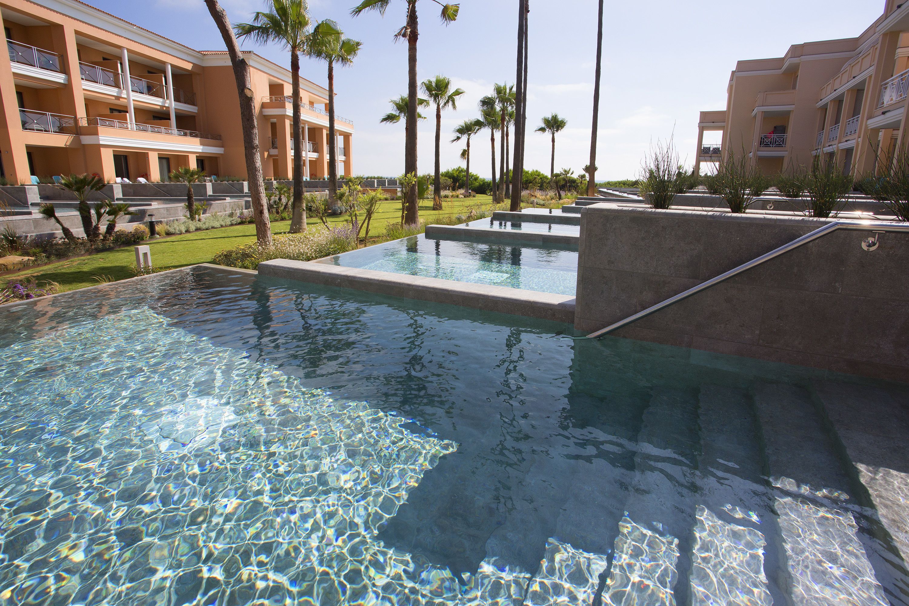 Una piscina dalle acque cristalline, circondata da palme e da un edificio con balconi.